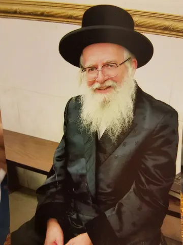 מוהרא״ש בכובע שחור ובחליפה שחורה, מחייך